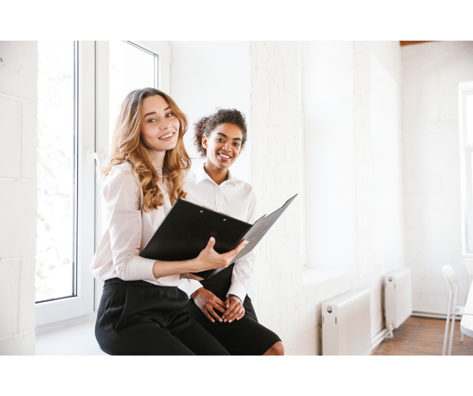 Two Employees who are happy working under a confident leader. They are sitting and smiling at the camera.