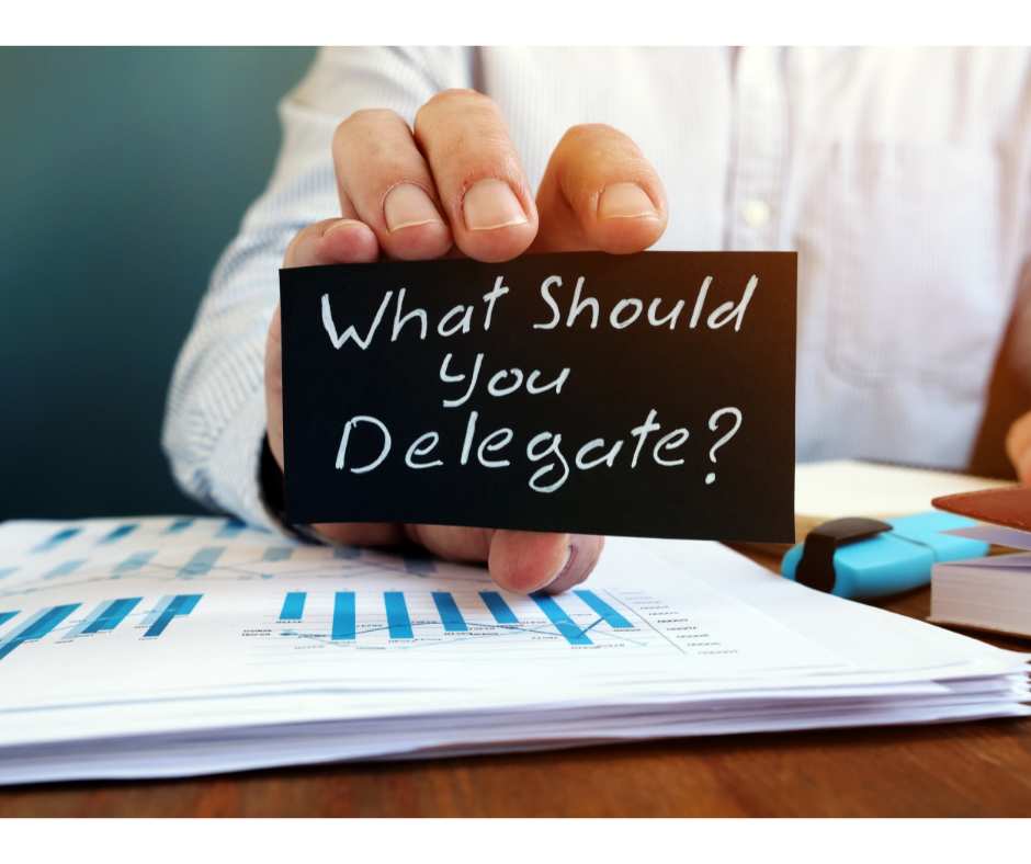 A hand holding a sign asking a question about what to delegate.