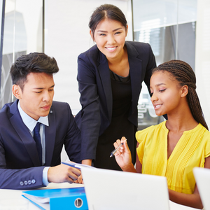 Three coworkers working together on an assignment. Two are sitting and the leaders is standing up smiling.